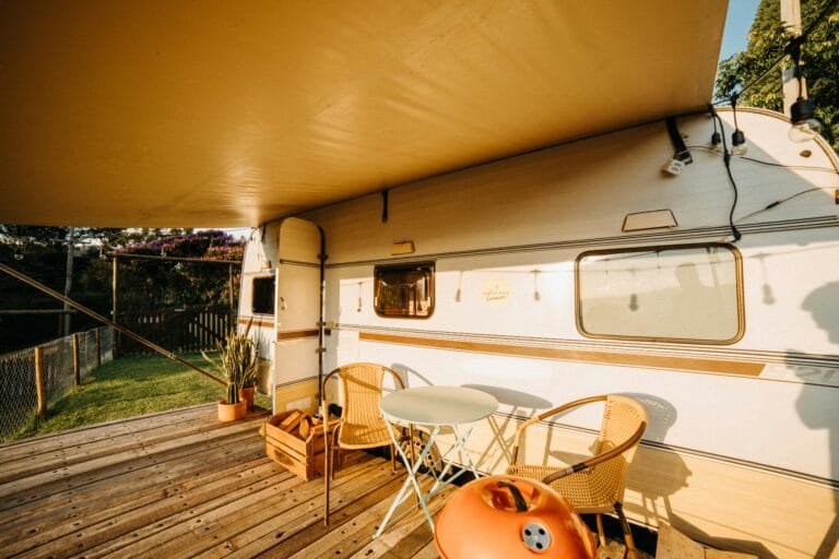 Sunlit caravan setup on a wooden deck with chairs and a canopy, perfect for summer camping.