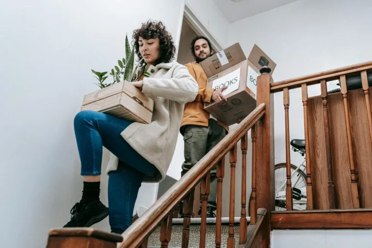 Couple carrying boxes and plants down stairs during a home move.