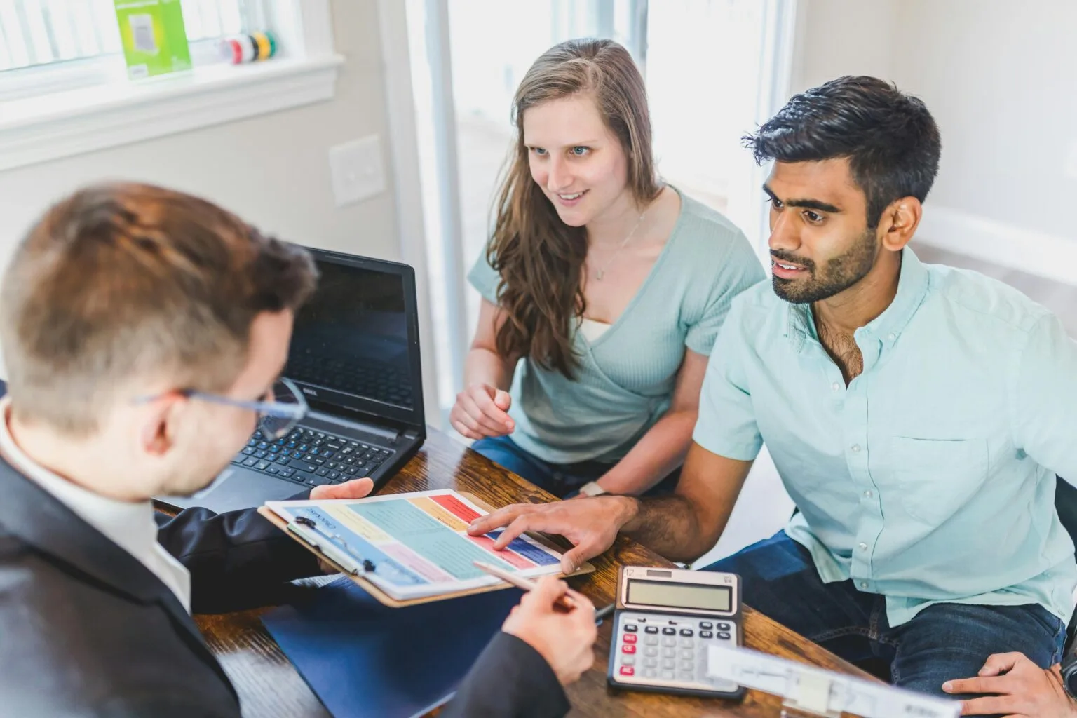 A couple consults with a real estate agent about buying a new home, papers and calculator on the table.