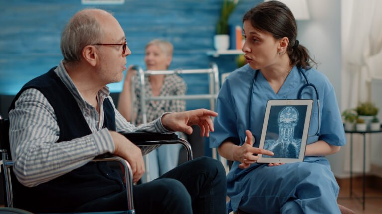 Medical assistant holding tablet with x ray scan for checkup with disabled man in nursing home. Nurse explaining radiography on digital device to senior patient sitting in wheelchair
