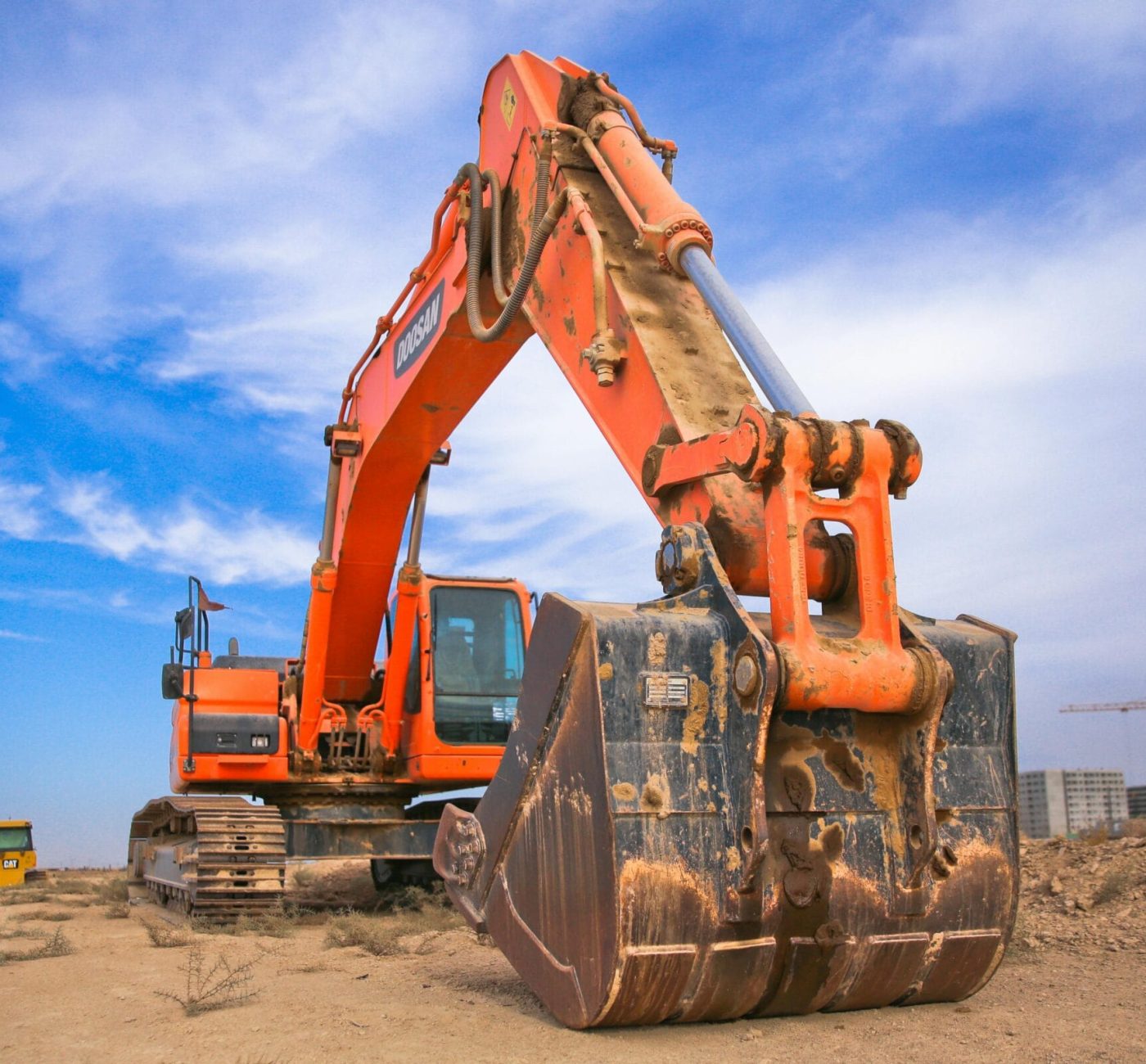 A large orange excavator working on a construction site under a blue sky.